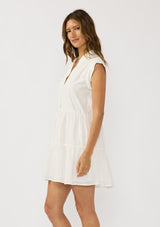 [Color: White] A side facing image f a brunette model earing a white baby doll mini dress an eyelet design, split v-neckline, button front, and rolled cap sleeves. 