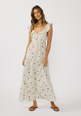[Color: Natural/Grey] A front facing image of a brunette model at the beach wearing white and grey striped maxi dress with floral embroidery. Featuring flutter sleeves, a button front, a tiered skirt, and a smocked back. 