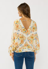 [Color: Ivory/Coral] A back facing image of a brunette model wearing an orange floral blouse with voluminous long sleeves, a tie detail, and v-neckline. 