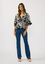 [Color: Black/Blush] A front facing image of a brunette model wearing a black and pink floral blouse with a v-neckline, adjustable drawstring waist, and flowy half length sleeves with ruched shoulder detail. 