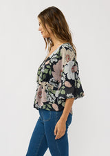 [Color: Black/Blush] A side facing image of a brunette model wearing a black and pink floral blouse with a v-neckline, adjustable drawstring waist, and flowy half length sleeves with ruched shoulder detail. 