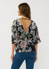 [Color: Black/Blush] A back facing image of a brunette model wearing a black and pink floral blouse with a v-neckline, adjustable drawstring waist, and flowy half length sleeves with ruched shoulder detail. 