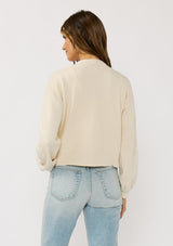 [Color: Ivory] A front facing image of a brunette model wearing an ivory cardigan with a collarless design, floral embroidery, and rib trims. 