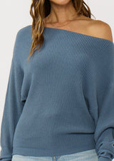 [Color: Heather Ocean] A front facing image of a brunette model wearing a blue waffle knit pullover sweater. With long sleeves, a relaxed fit, and a wide neckline that can be worn off the shoulder.