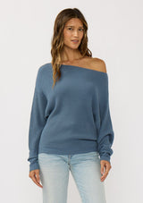 [Color: Heather Ocean] A front facing image of a brunette model wearing a blue waffle knit pullover sweater. With long sleeves, a relaxed fit, and a wide neckline that can be worn off the shoulder.