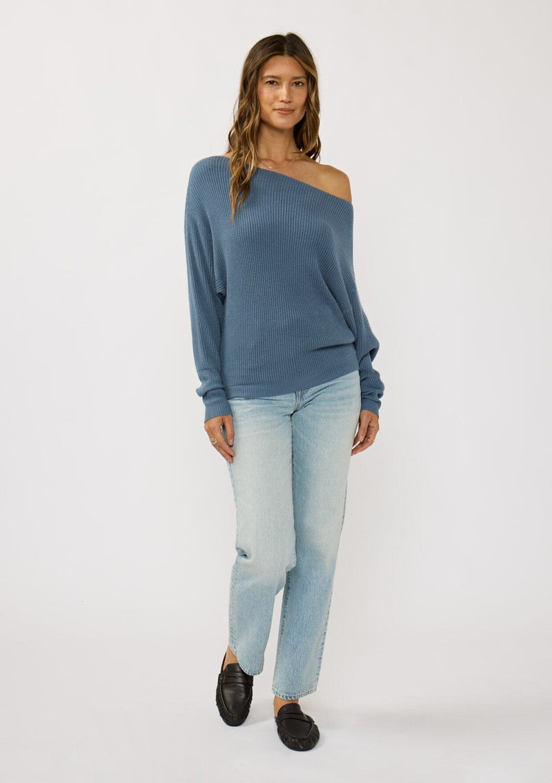 [Color: Heather Ocean] A front facing image of a brunette model wearing a blue waffle knit pullover sweater. With long sleeves, a relaxed fit, and a wide neckline that can be worn off the shoulder.
