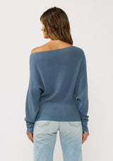 [Color: Heather Ocean] A  back facing image of a brunette model wearing a blue waffle knit pullover sweater. With long sleeves, a relaxed fit, and a wide neckline that can be worn off the shoulder.