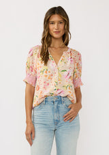 [Color: Natural/Fuchsia] A front facing image of a brunette model wearing a pink floral top with a button front and puff sleeves with smocked cuffs. A pretty spring casual top paired with denim. 