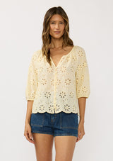 [Color: Yellow] A front facing image of a brunette model wearing a floral eyelet embroidered top with half sleeves, a button front, and scallop trimmed hem. 