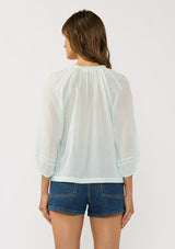 [Color: Mint] A back facing image of a brunette model wearing a sheer mint blouse with lace trims. Featuring a round neckline, button front, and 33/4 length sleeves with elastic cuffs. A lightweight boho cotton blouse. 