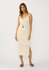 [Color: Natural] A front facing image of a brunette model wearing a beige pointelle knit midi skirt with side slits and a ribbed elastic waistband. Styled with a matching knit tank top. 