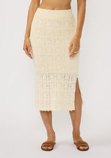 [Color: Natural] A front facing image of a brunette model wearing a beige pointelle knit midi skirt with side slits and a ribbed elastic waistband. 