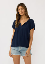 [Color: Navy] A front facing image of a brunette model wearing a navy blue puff sleeve top with a split v-neckline and neck ties. 