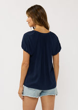 [Color: Navy] A back facing image of a brunette model wearing a navy blue puff sleeve top with a split v-neckline and neck ties. 