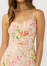 [Color: Natural/Fuchsia] A detail image of brunette model wearing a pink floral midi dress with adjustable spaghetti straps, a smocked back, and a pleated hem detail. 