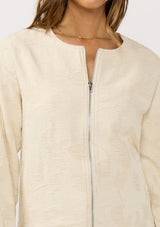 [Color: Natural] A detail image of a brunette model wearing a beige jacquard jacket with a collarless design, zip-up front, and side pockets. A lightweight jacket for the spring season. 
