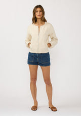 [Color: Natural] A front facing image of a brunette model wearing a beige jacquard jacket with a collarless design, zip-up front, and side pockets. A lightweight jacket for the spring season. 