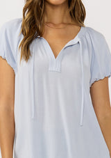 [Color: Dusty Lilac] A detail image of a brunette model wearing a light purple puff sleeve top with a split v-neckline and neck ties. 