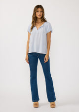 [Color: Dusty Lilac] A front facing image of a brunette model wearing a light purple puff sleeve top with a split v-neckline and neck ties. 