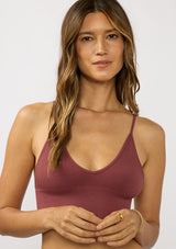[Color: Burgundy] A detail image of a brunette model wearing a basic burgundy bralette cami with a slim stretchy fit and a v-neckline.