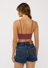 [Color: Burgundy] A back facing image of a brunette model wearing a basic burgundy bralette cami with a slim stretchy fit and a v-neckline.