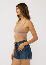[Color: Taupe] A side facing image of a brunette model wearing a basic taupe bralette cami with a slim stretchy fit and a v-neckline.