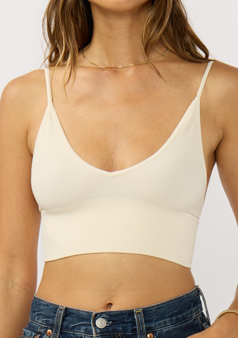 [Color: Cream] A detail image of a brunette model wearing a basic off white bralette cami with a slim stretchy fit and a v-neckline.