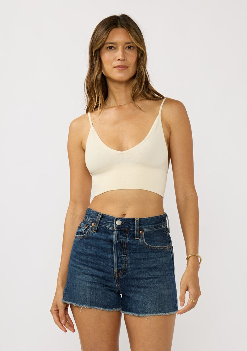 [Color: Cream] A front facing image of a brunette model wearing a basic off white bralette cami with a slim stretchy fit and a v-neckline.
