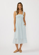 [Color: Light Blue] A front facing image of a brunette model wearing a light blue eyelet midi dress with ruffled straps, slim elastic bodice, and side pockets. The perfect spring time dress. 