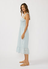 [Color: Light Blue] A side facing image of a brunette model wearing a light blue eyelet midi dress with ruffled straps, slim elastic bodice, and side pockets. The perfect spring time dress. 