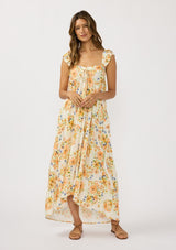 [Color: Ivory/Coral] A front facing image of a brunette model wearing an orange floral maxi dress with an elastic shoulder strap, ruffle sleeves, a sweetheart neckline with tie detail, and a flowy tiered skirt. A flowy casual spring dress. 