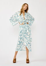 [Color: Ivory/Dark Teal] A front facing image of a blonde model wearing a white and teal tropical floral print wrap skirt, tie waist, and a smocked back. Styled with a matching tie front top. Perfect for vacation or casual outings. 