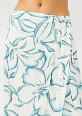 [Color: Ivory/Dark Teal] A detail image of a blonde model wearing a white and teal tropical floral print wrap skirt, tie waist, and a smocked back. Styled with a matching tie front top. Perfect for vacation or casual outings. 