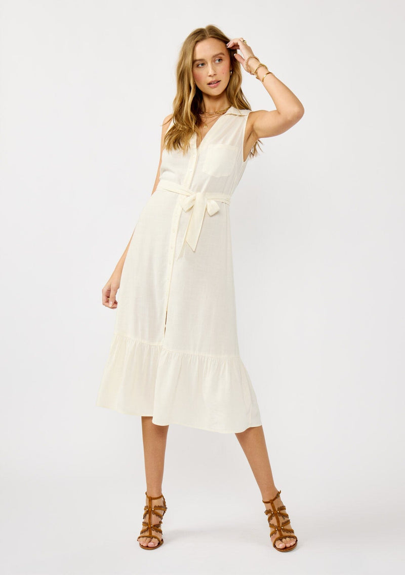 [Color: Natural] A front facing image of a blonde model wearing an off white sleeveless shirt dress with a collared neckline, button front, and a self tie waist belt. 