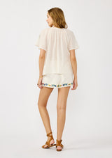 [Color: Cream] A back facing image of a blonde model wearing cream floral embroidered short crafted in soft cotton with  matching top. Featuring a smocked waist, a drawstring, and side pockets. 