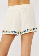 [Color: Cream] A back facing image of a cream floral embroidered short crafted in soft cotton. Featuring a smocked waist, a drawstring, and side pockets. 