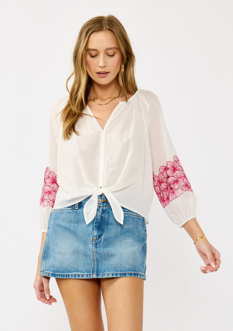 [Color: Off White/Fuchsia] A front-facing image of a blonde model wearing a white sheer tie-front top, featuring delicate pink floral embroidered cutouts along the sleeves.