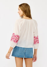 [Color: Off White/Fuchsia] A back-facing image of a blonde model wearing a white sheer tie-front top, featuring delicate pink floral embroidered cutouts along the sleeves.