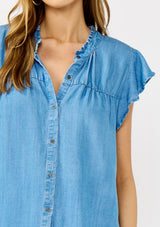 [Color: Light Denim Blue] A detail image of a blonde model wearing a soft blue denim Tencel top featuring a button front, flutter sleeves, and ruffle trim accents. A lightweight and flowy summer top.