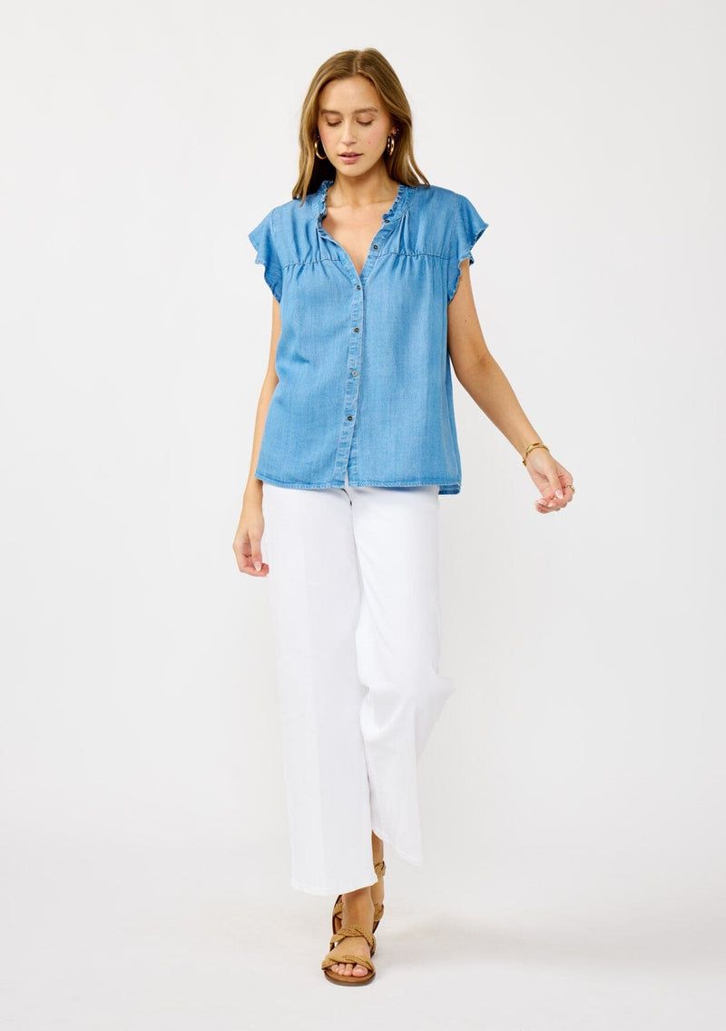 [Color: Light Denim Blue] A front facing image of a blonde model wearing a soft blue denim Tencel top featuring a button front, flutter sleeves, and ruffle trim accents. A lightweight and flowy summer top.
