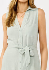 [Color: Grey Mist] A detail mage of a blonde model wearing a light green sleeveless shirt dress with a collared neckline, button front, and a self tie waist belt. 