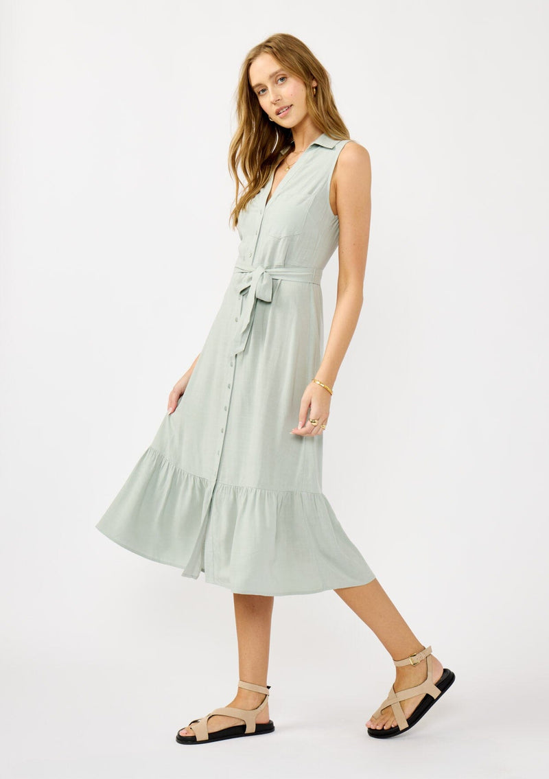 [Color: Grey Mist] A front facing image of a blonde model wearing a light green sleeveless shirt dress with a collared neckline, button front, and a self tie waist belt. 