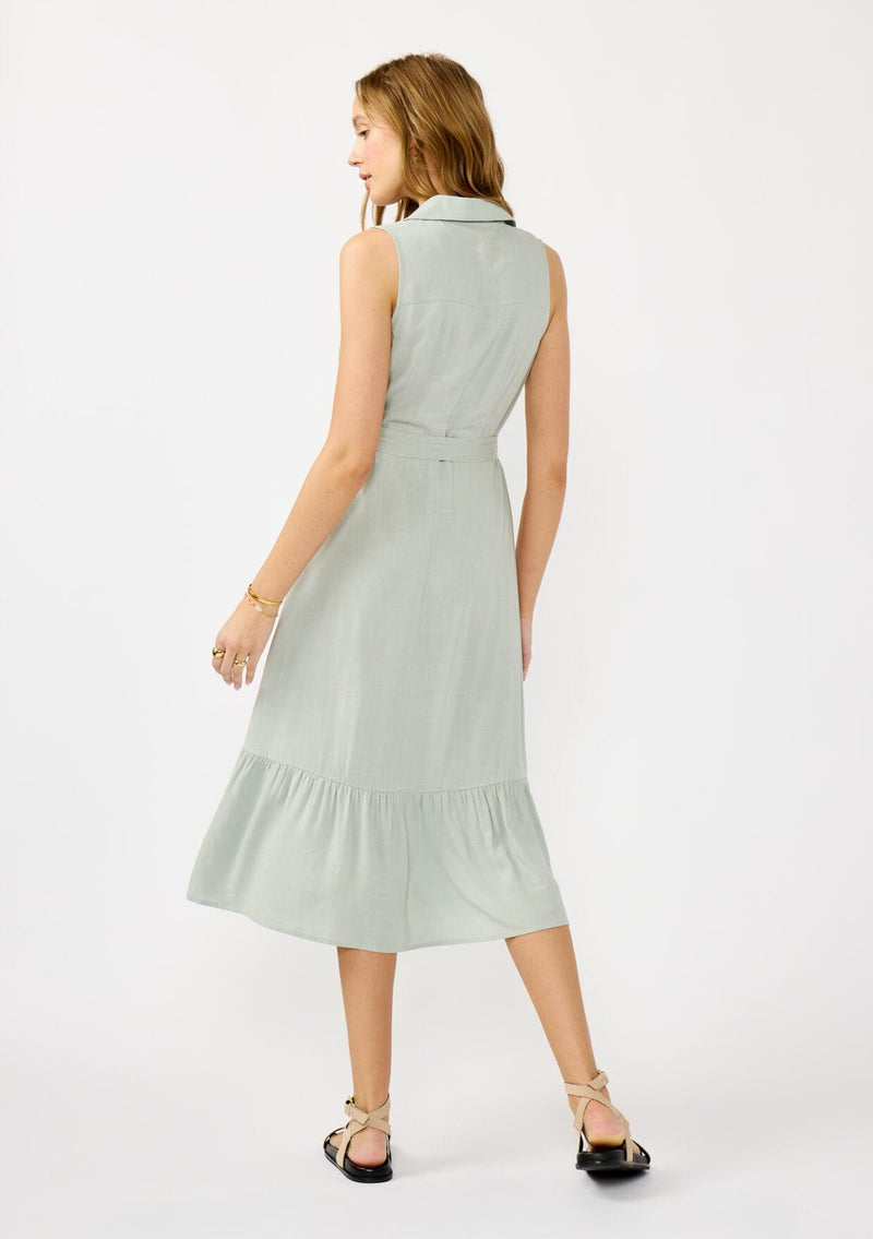 [Color: Grey Mist] A back facing image of a blonde model wearing a light green sleeveless shirt dress with a collared neckline, button front, and a self tie waist belt. 