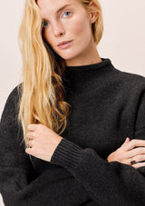 [Color: Charcoal] A blonde model wearing a charcoal sweater with an elegant funnel neck, a concealed zip closure at the back neck, and contrast ribbed details. A basic cold weather sweater for the fall season. 