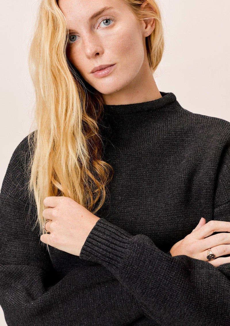 [Color: Charcoal] A blonde model wearing a charcoal sweater with an elegant funnel neck, a concealed zip closure at the back neck, and contrast ribbed details. A basic cold weather sweater for the fall season. 