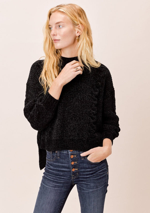 [Color: Black] A blonde model wearing a cozy cable knit sweater made with super soft chenille. Featuring a flattering ribbed funnel neck and a chic high low hemline with side vents. 