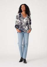 [Color: Natural/Navy] A full body front facing image of a brunette model wearing a flowy chiffon bohemian blouse in a blue and white floral print. With voluminous long sleeves, ruffle details, and a v neckline with doubles ties. 
