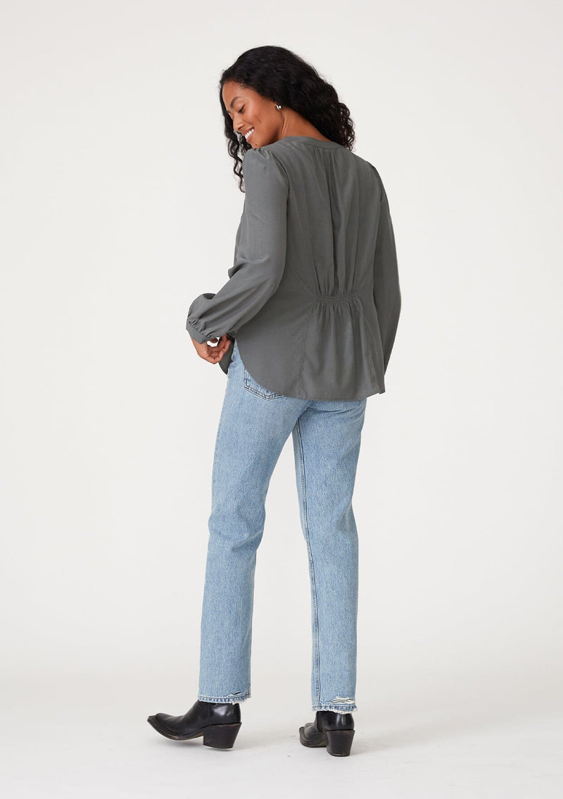 [Color: Moss] A full body back facing image of a brunette model wearing a moss green blouse with a v neckline, long sleeves, a relaxed fit, and a smocked detail at the back.