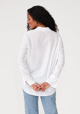 [Color: Chalk] A back facing image of a brunette model wearing a white button front blouse with a tie waist detail. With a button front, a deep v neckline, long sleeves, and long wrist cuffs with a button closure. 