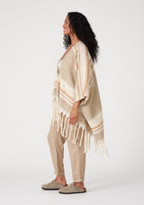 [Color: Taupe/Rust] A side facing image of a brunette model wearing a soft sweater shawl in a taupe and cream stripe. With a fringed hemline, a mid length silhouette, an open front, and long sleeves. 